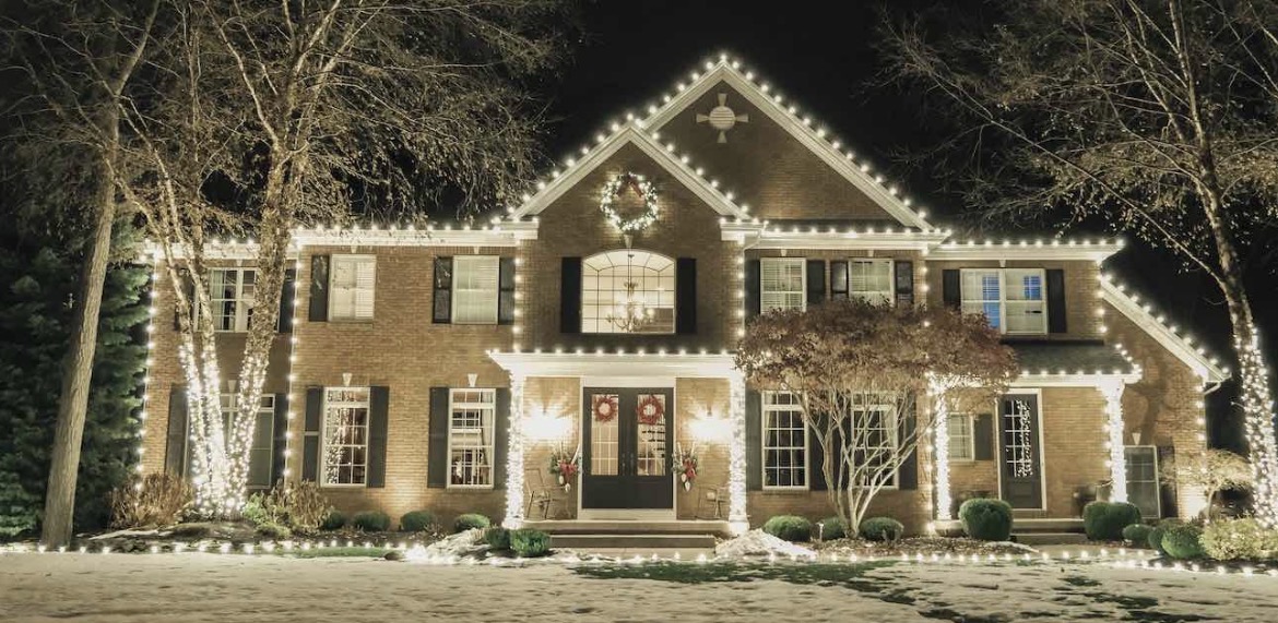 Brick colonial home in Short Hills NJ with its full roofline lit in warm white C9 bulbs, wreaths on the doors, wrapped front-yard trees and a lit shrub line in the snow