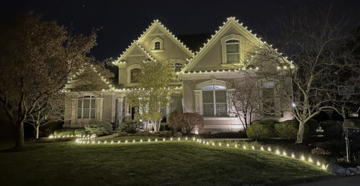 Ground stake lights outlining the front lawn and walkway of a Short Hills NJ home with warm white roofline lighting above