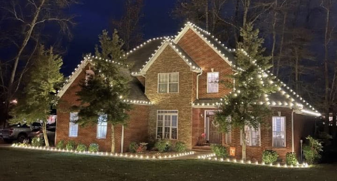 Brick two-story home in Short Hills NJ with a warm white lit roofline and ground stake lights running along the edge of the front lawn