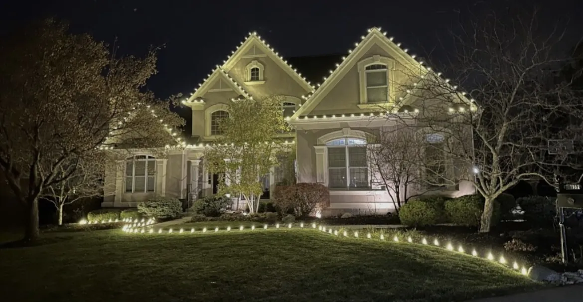 Ground stake lights outlining the front lawn and walkway of a Short Hills NJ home with warm white roofline lighting above