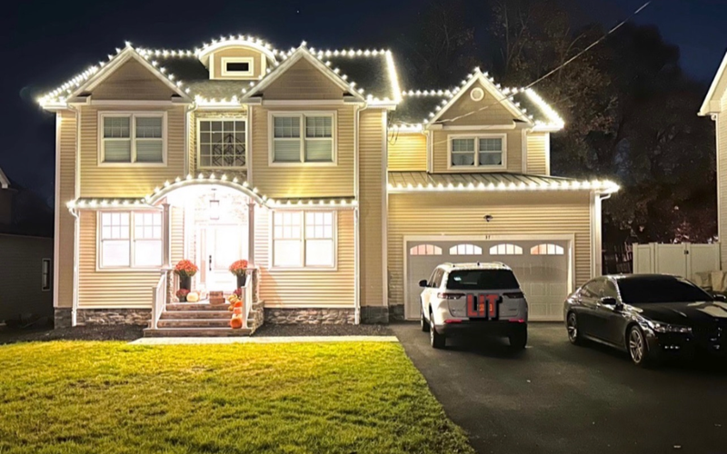 Two-story Short Hills NJ colonial outlined in bright C9 Christmas lights along every roofline and porch