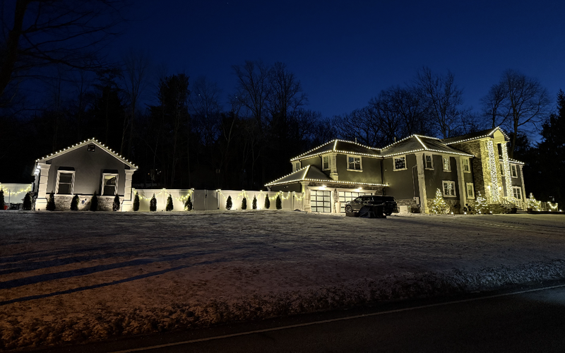 Large Short Hills NJ property with lights on the main house, garage and lined driveway