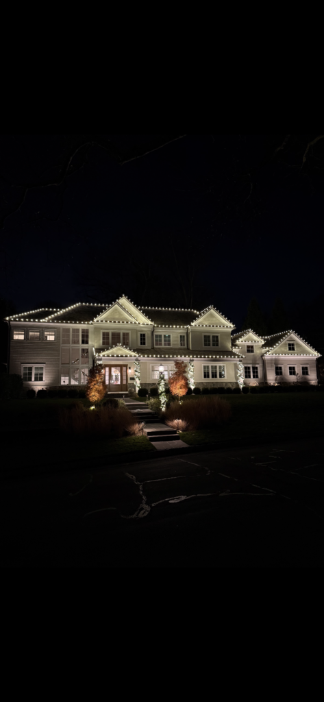 Estate home in Short Hills NJ outlined in warm white Christmas lights with uplit landscaping
