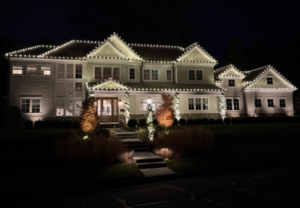 Estate home in Short Hills NJ outlined in warm white Christmas lights with uplit landscaping