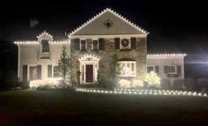 Short Hills NJ colonial with roofline Christmas lights and a lighted walkway across the lawn