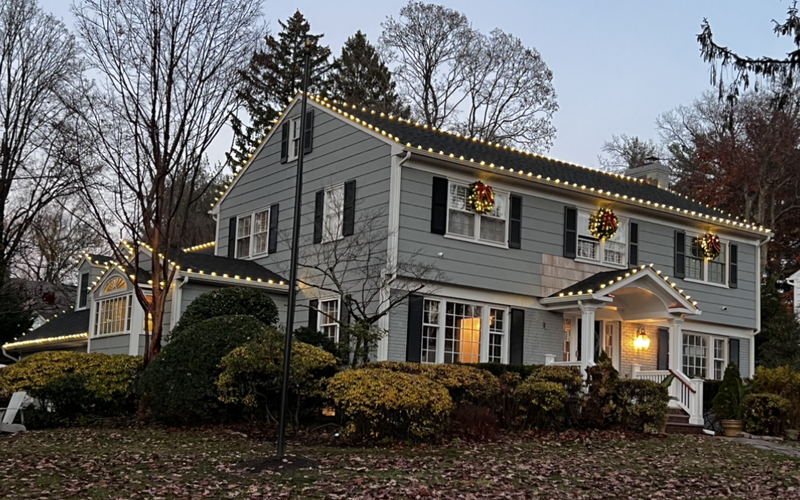 Short Hills NJ colonial with roofline C9 lights and holiday wreaths on the front windows at dusk