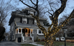 Short Hills NJ home with roofline lights and a large tree wrapped in warm white lights