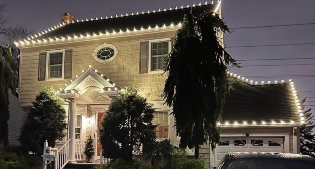 Short Hills NJ colonial with warm white roofline lights and lit evergreens at the entry