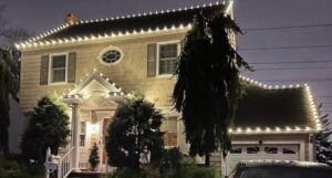 Short Hills NJ colonial with warm white roofline lights and lit evergreens at the entry